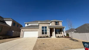 Two-story brick house with a white garage door, dark shutters, and a small front porch under a clear blue sky