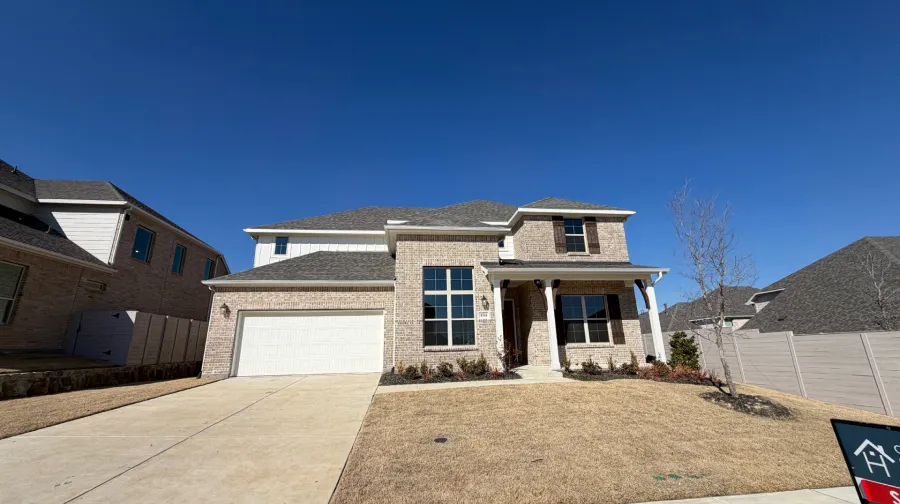 Two-story brick house with a white garage door, dark shutters, and a small front porch under a clear blue sky